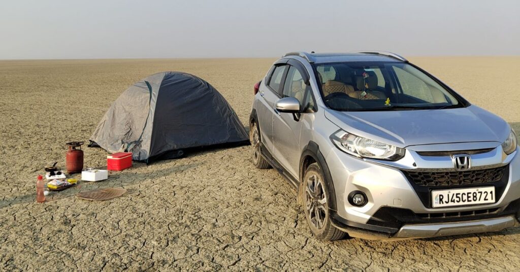 Camping setup with a tent and car on the dry salt flats of Sambhar Salt Lake, Rajasthan, capturing a peaceful desert camping experience in an open landscape.