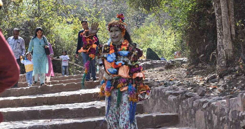 A Behrupiya artist at Ranthambore Fort, Rajasthan, dressed in a vibrant traditional costume, greeting visitors with a painted face and floral decorations while performing on stone steps